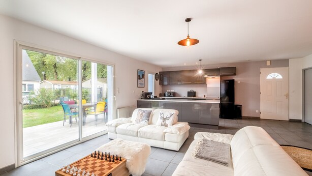 A modern living room with a sofa, a coffee table with a chessboard, and a kitchen in the background.