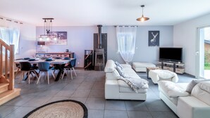 A modern living room with a sofa set, a dining area with a table and chairs, a fireplace, and a television.
