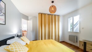 A bedroom with a large bed, a bedside table, a lamp, a radiator, and a window.