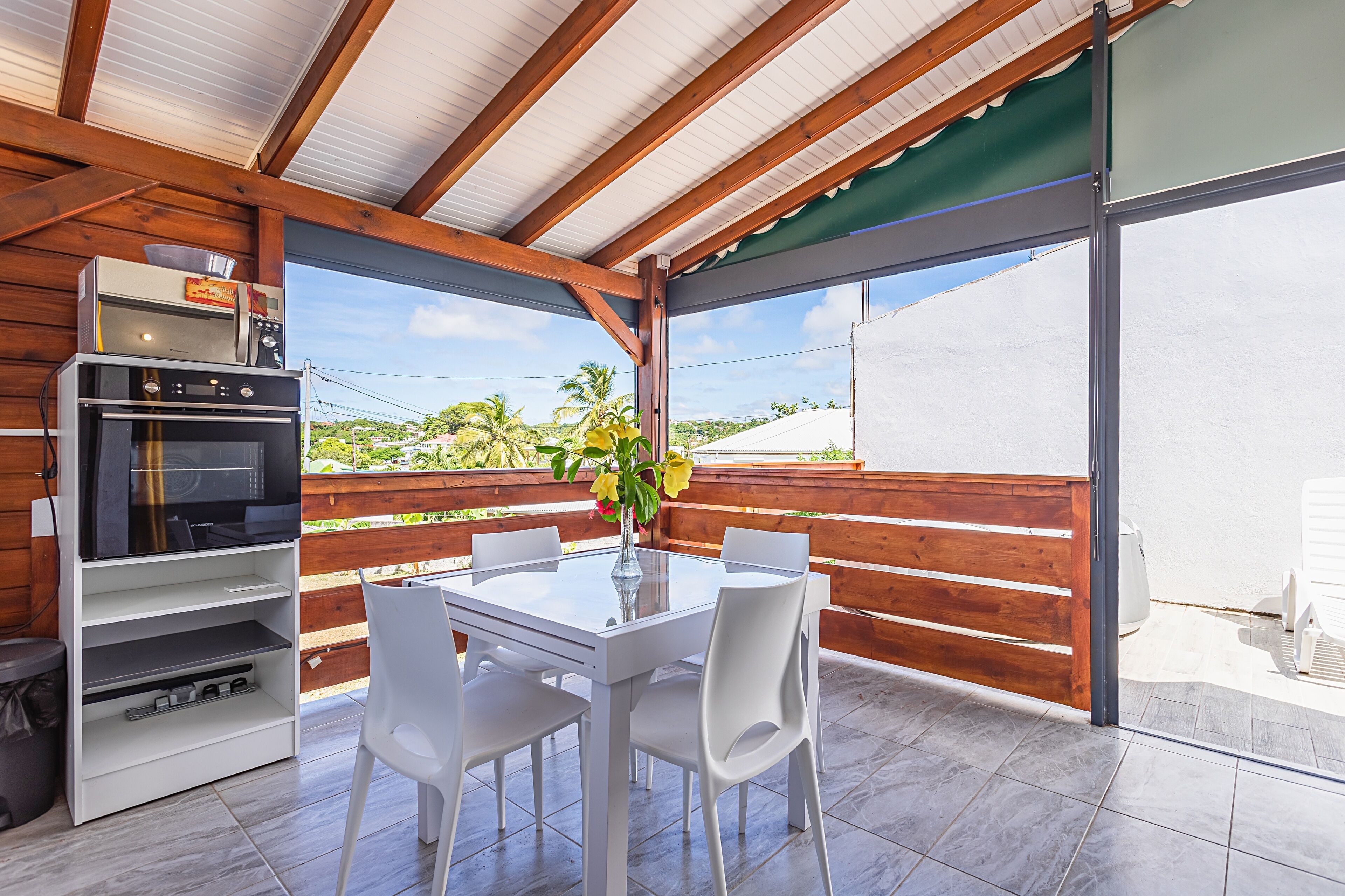 An outdoor dining area with a white table and chairs, a pizza oven, and a TV on a shelf.