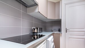 A modern kitchen with grey tiles, a built-in stove, a washing machine, and a white door.