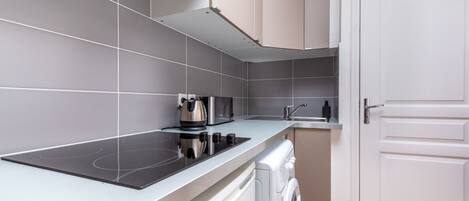 A modern kitchen with grey tiles, a built-in stove, a washing machine, and a white door.