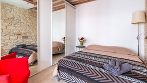A bedroom with a mirrored closet, a bed with patterned bedding, a red chair, and a bedside lamp.