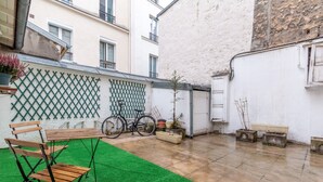A courtyard with a green artificial turf, a wooden bench, and a bicycle.