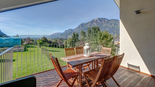 Ein Balkon mit Holztisch und Stühlen, einer Laterne und Blick auf Berge.