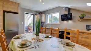 Eine moderne Küche mit Esstisch für vier Personen, Holzschränken, einem eingebauten Backofen und einem an der Wand montierten Fernseher.