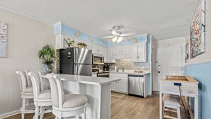 A modern kitchen with white cabinetry, a central island, bar stools, a refrigerator, microwave, oven, and a ceiling fan. - Ocean Forest Villas 115C- 2 Br Condo in Myrtle Beach (Myrtle Beach)
