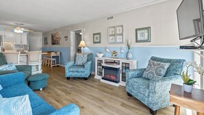 A living room with blue patterned furniture, a fireplace, and wall art. - Ocean Forest Villas 115C- 2 Br Condo in Myrtle Beach (Myrtle Beach)