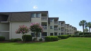 A row of multi-story residential buildings with balconies, a well-maintained lawn, and flowering shrubs. - Ocean Forest Villas 115C- 2 Br Condo in Myrtle Beach (Myrtle Beach)