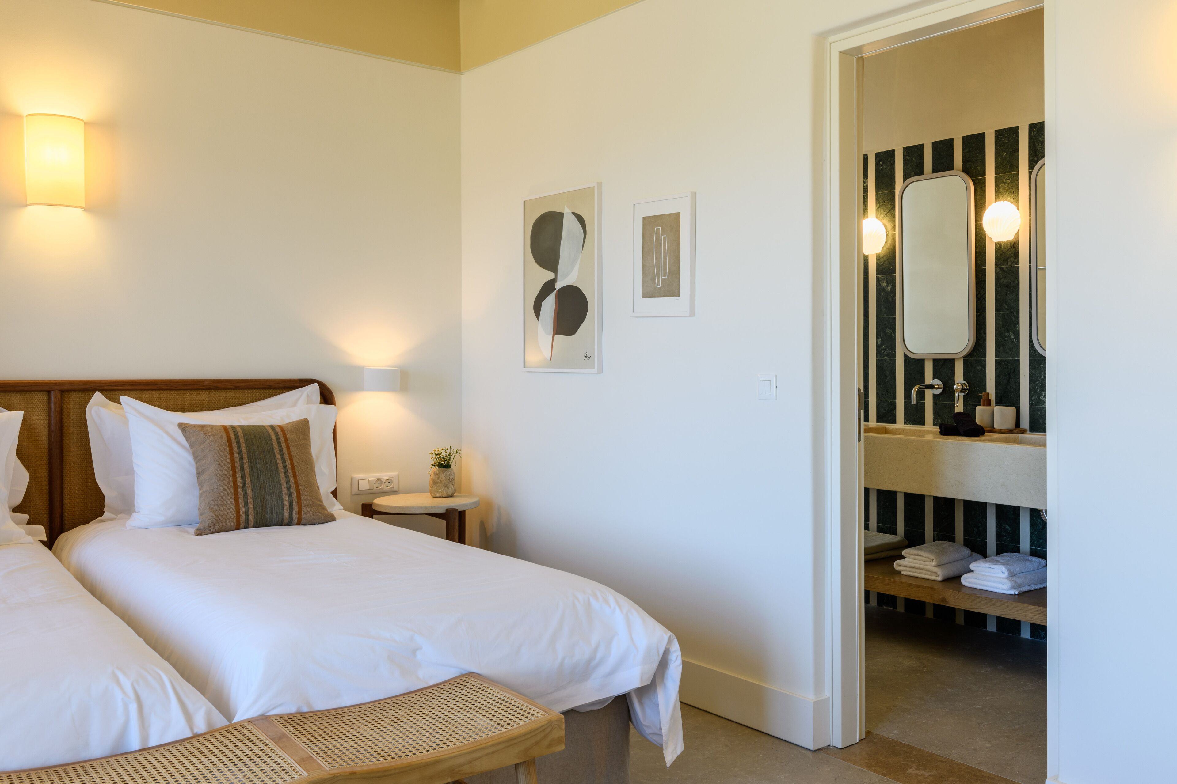 Une chambre d’hôtel avec deux lits, une petite table, une table de chevet et une salle de bain équipée d’un miroir et d’un porte-serviettes.