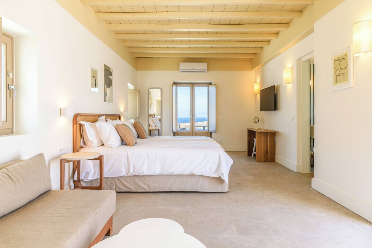 A bedroom with a bed, a sofa, a small table, and a TV.