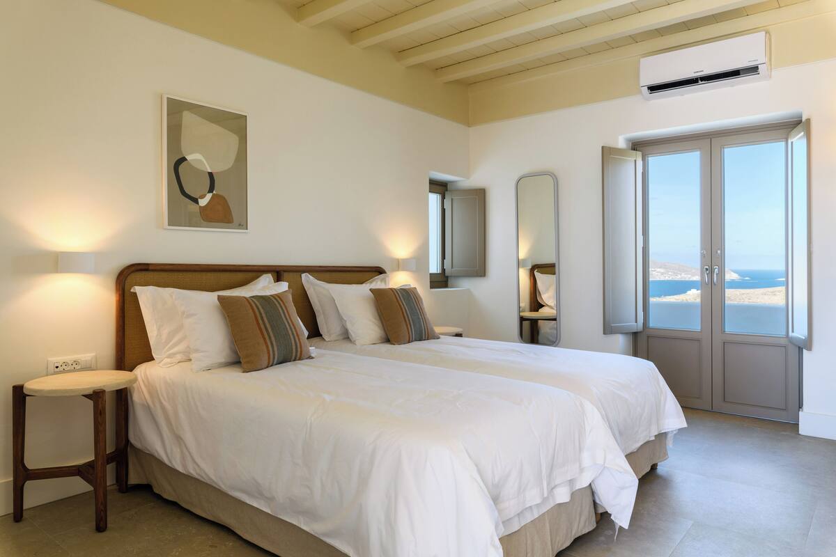 A bedroom with a large bed, bedside tables, a mirror, and a view of the sea.