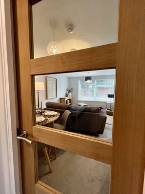 A room with a wooden door, a dining table set for two, a sofa, and a lamp. - BookedUK - Lovely 2BR Flat in Hoddesdon (Hoddesdon)