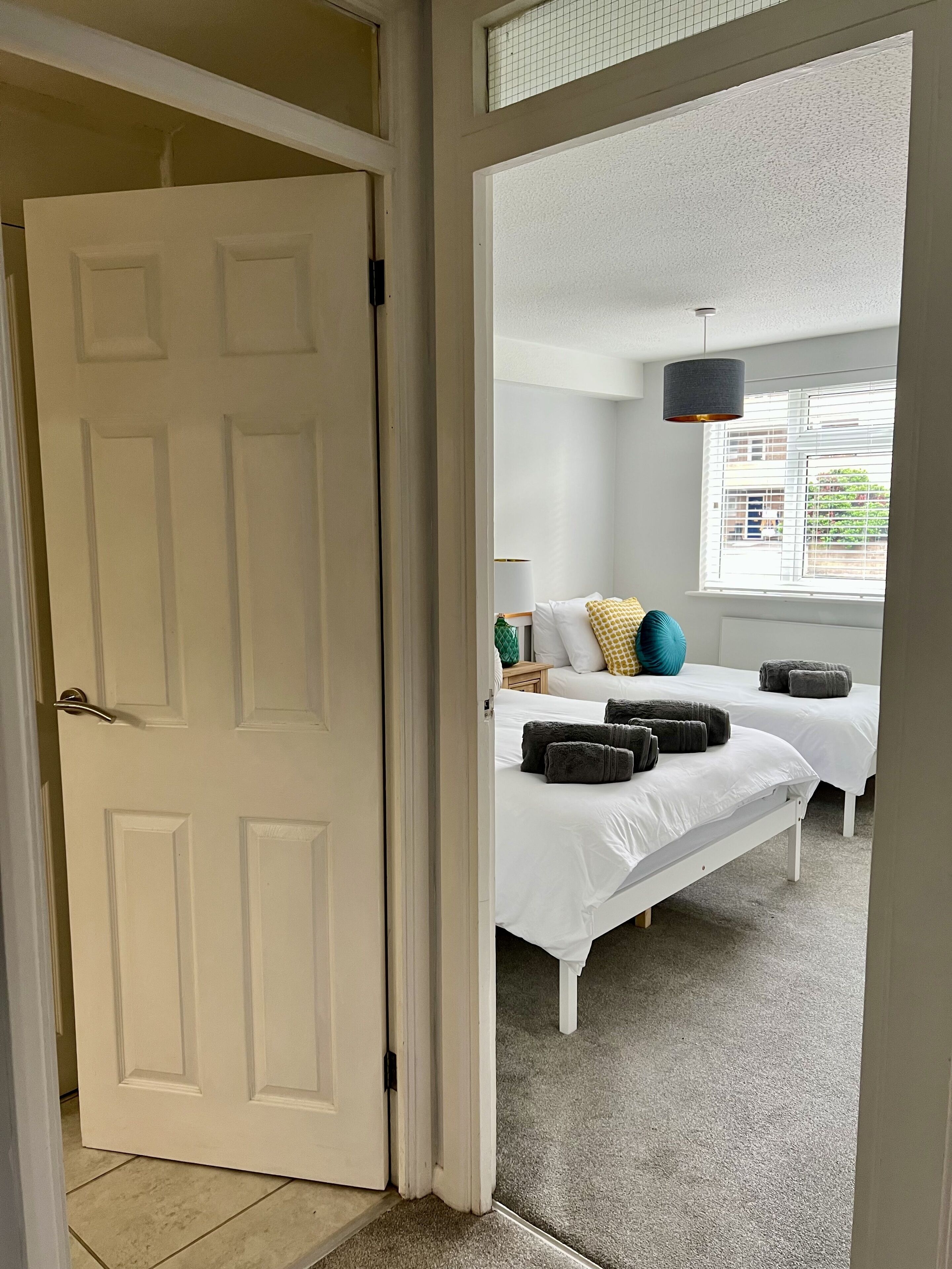 Une chambre d’hôtel avec deux lits, une fenêtre avec des stores, une lampe et une porte.
