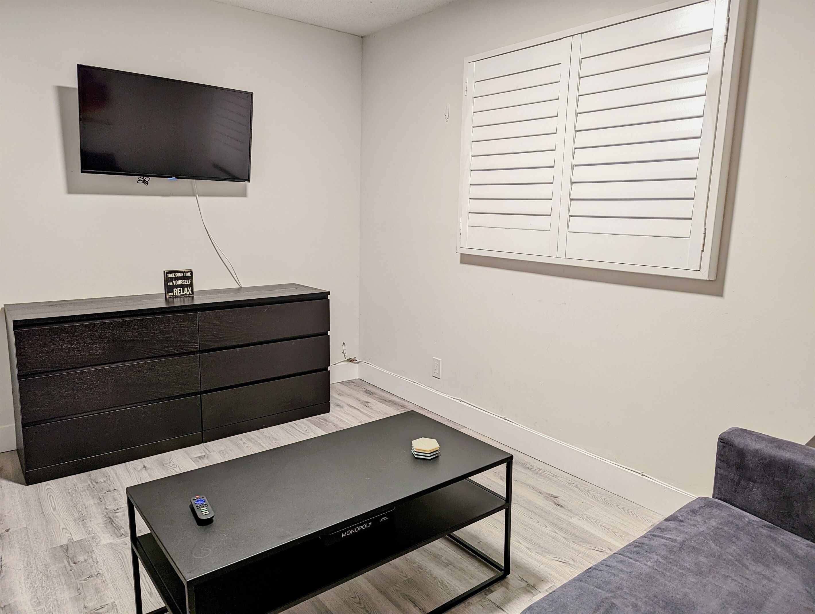A modern living room with a flat-screen TV mounted on the wall, a dark wooden dresser, a black coffee table, and a gray sofa.