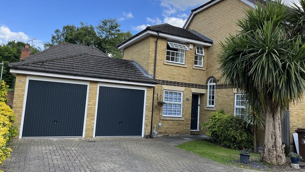 A two-story house with a garage, brick exterior, and a well-maintained garden. - SleepNeat (Ascot)