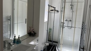 A modern bathroom with a glass-enclosed shower, a vanity with a mirror, and toiletries. - SleepNeat (Ascot)
