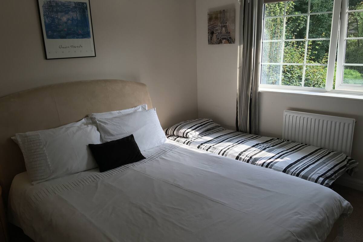 A bedroom with a large bed, two smaller beds, a headboard, and a window with curtains.