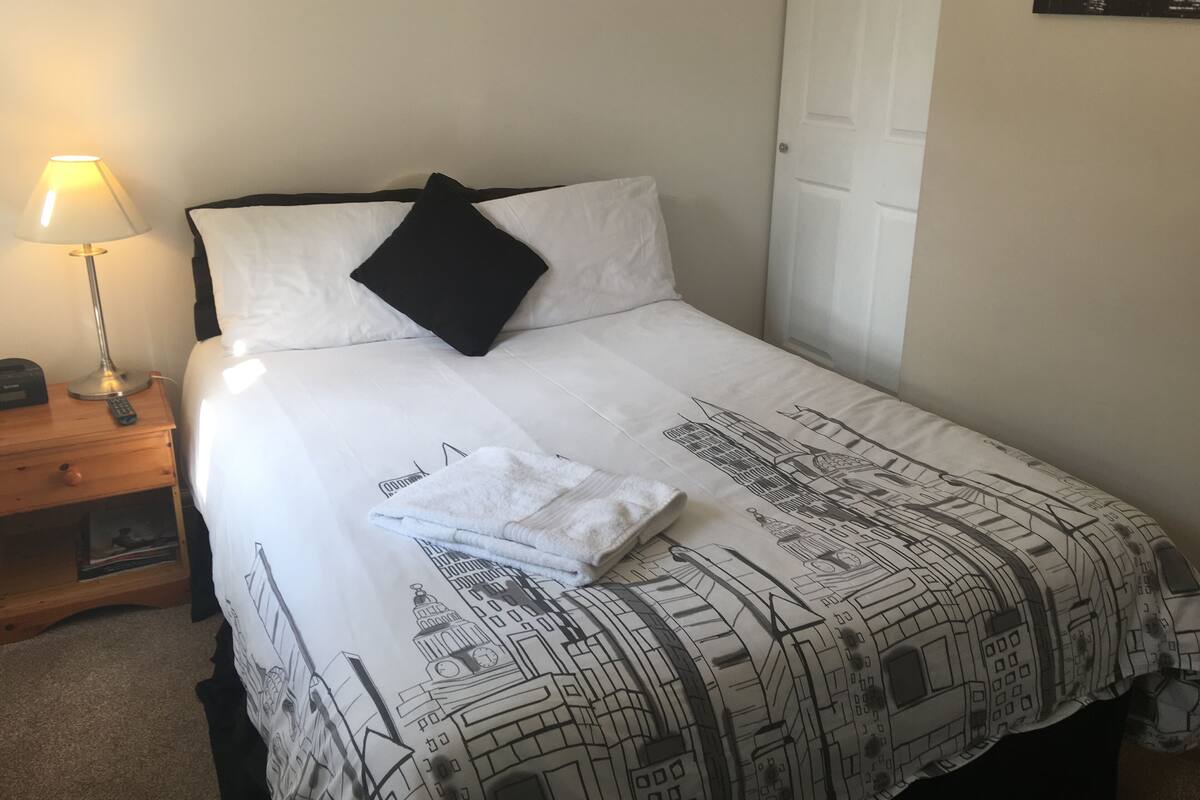 A neatly made bed with a patterned bedspread, a black pillow, and a folded white towel on the bed.
