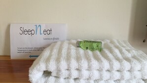 A white towel on a wooden surface with a green bottle and a sign that reads "Sleep n Eat" indicating a hotel amenity. - SleepNeat (Ascot)