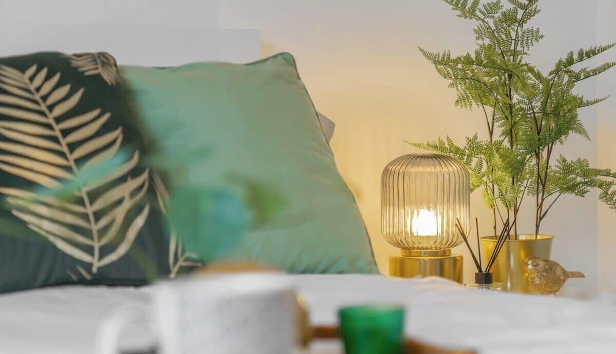 Ein Bett mit einem grünen Kopfkissen, einer Nachttischlampe und einer kleinen Pflanze.
