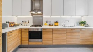 A modern kitchen with wooden cabinets, a stainless steel range hood, a built-in oven, a sink, and a countertop with various items. - 4BR-Madejski Stadium-Royal Berk Hosp-By Tempstay (Reading)