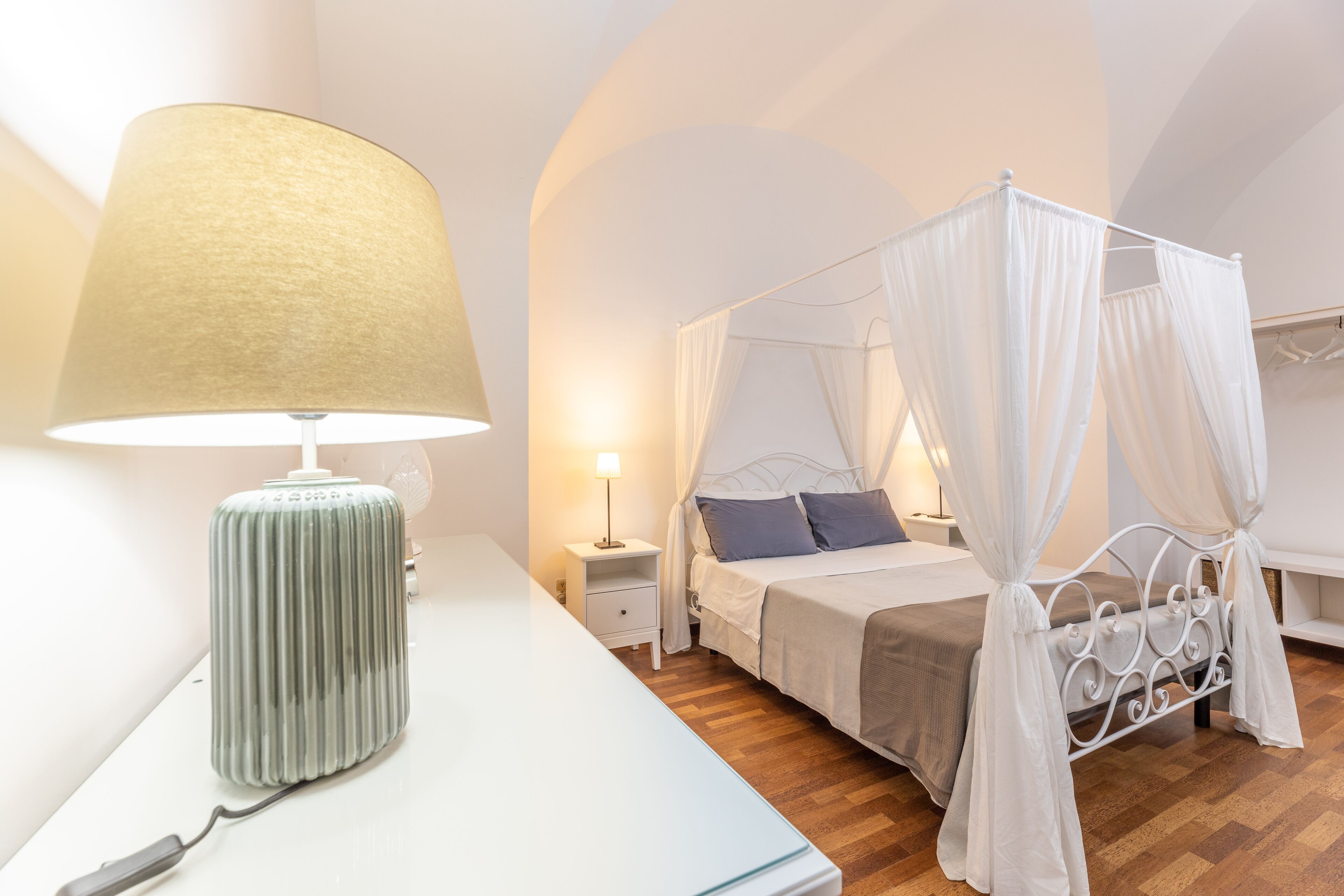 Un dormitorio con una cama, una mesita de noche, una lámpara y un dosel blanco sobre la cama.