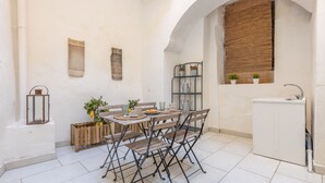 A compact kitchen with a dining table, chairs, a small cabinet, and a window with a bamboo blind. - Corte Tiso (Lecce)