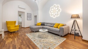 A living room with a modern design, featuring a sofa, armchair, and a decorative wall light. - Corte Tiso (Lecce)