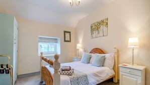 Ein Schlafzimmer mit einem hölzernen Bett, zwei Nachttischlampen, einem Fenster mit Jalousien, einem Heizkörper und einer Tür mit Griff.