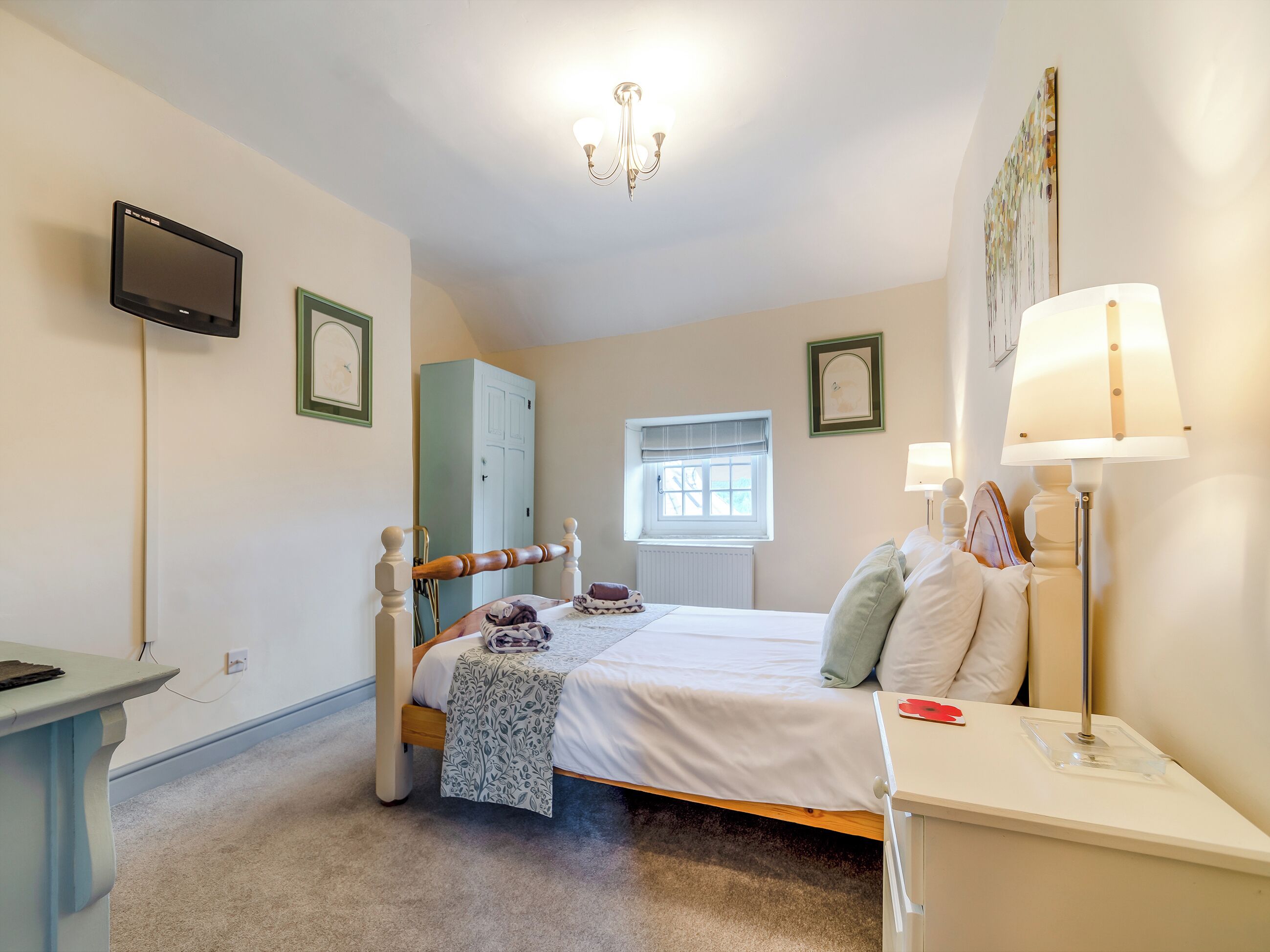 Ein Schlafzimmer mit Bett, Nachttisch, Lampe, Kleiderschrank und Fernseher an der Wand.