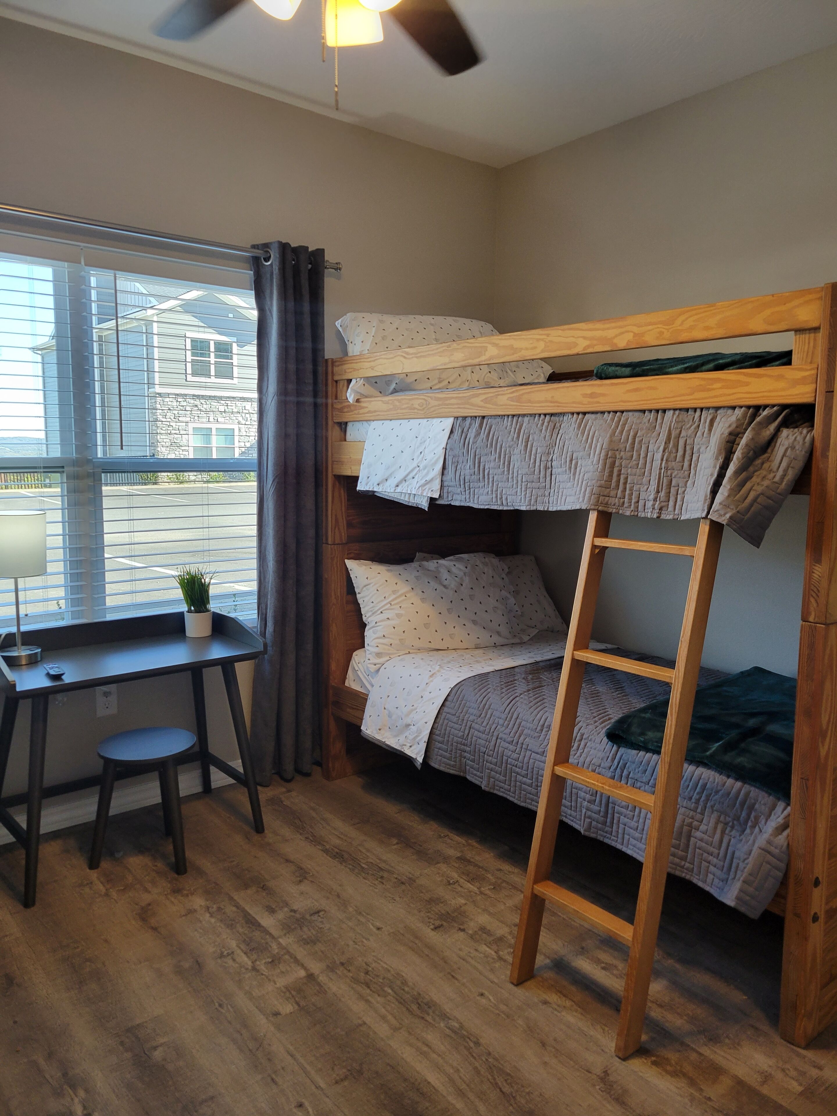 A bunk bed with a ladder, a desk with a chair, a small plant, and a window with curtains.