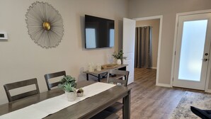A dining area with a dark wooden table, white tablecloth, and two chairs. A flat-screen TV is mounted on the wall above the table. - New Branson Condo!! (Branson)