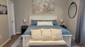 A bedroom with a bed, bedside tables, a bench, a painting, and a mirror. - New Branson Condo!! (Branson)