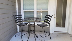 A small outdoor patio with a metal table and two chairs, a window with blinds, and a door. - New Branson Condo!! (Branson)