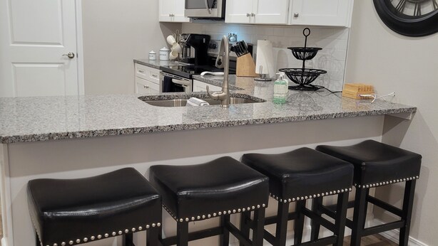 A kitchen with white cabinets, a stainless steel sink, and a black clock on the wall. - New Branson Condo!! (Branson)