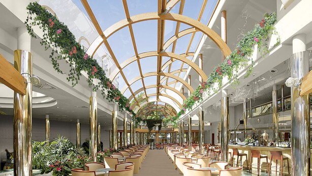 A spacious indoor area with a high ceiling and a glass dome structure. There are rows of seating along the sides and a central walkway. - Ona Palmira Paradise (Calvia)