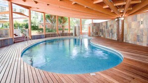 An indoor swimming pool with wooden decking, large windows, and a stone wall. - Ona Palmira Paradise (Calvia)