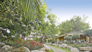 A garden pathway with large rocks and greenery, leading to a covered seating area with people. - Ona Palmira Paradise (Calvia)