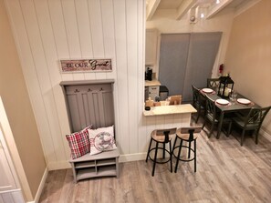 A cozy kitchen with a dining area, wooden bench, and a sign that reads "BE OUR GUEST".