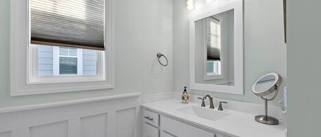 A bathroom with a window, white vanity, mirror, and light fixture.