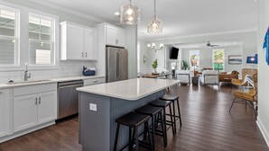 Une cuisine moderne avec des meubles blancs, un îlot central doté de tabourets et un éclairage suspendu.