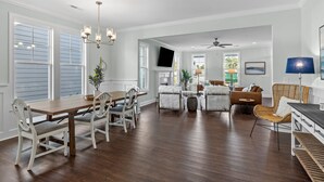 Un salon spacieux avec une table à manger en bois, des chaises blanches et une grande fenêtre.
