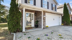 A two-story house with a stone facade, a garage, and a front porch with a potted plant. - Spacious King Suite w/ Game Room, Fire Pit & Patio (Lexington)