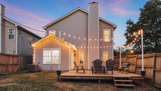 A two-story house with a covered patio area, string lights, and outdoor furniture. - Spacious King Suite w/ Game Room, Fire Pit & Patio (Lexington)