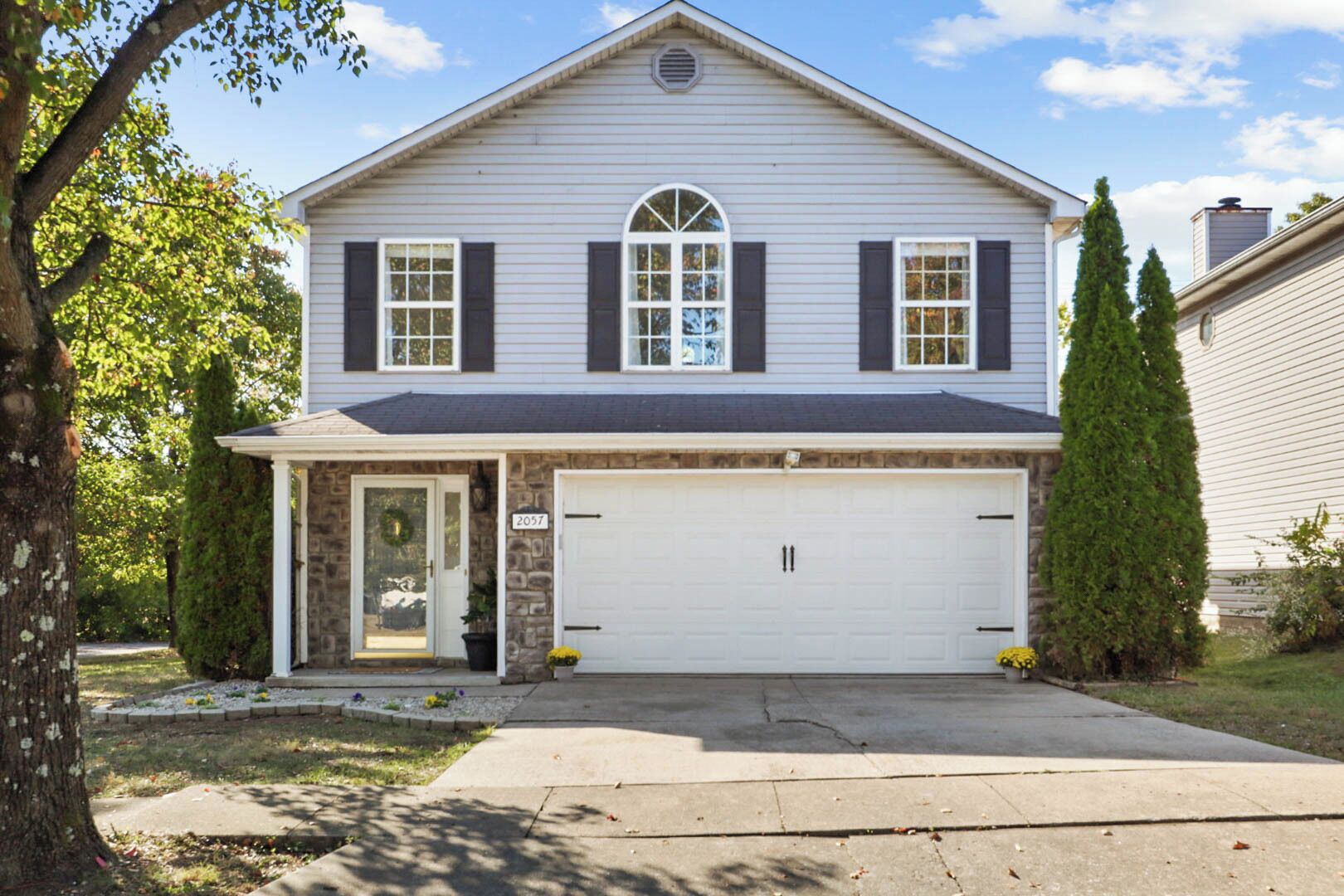 Une maison à deux étages avec un garage, un porche à l’avant et des fondations en pierre.