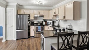 A modern kitchen with stainless steel appliances, wooden cabinets, and a central island with chairs. - Spacious King Suite w/ Game Room, Fire Pit & Patio (Lexington)