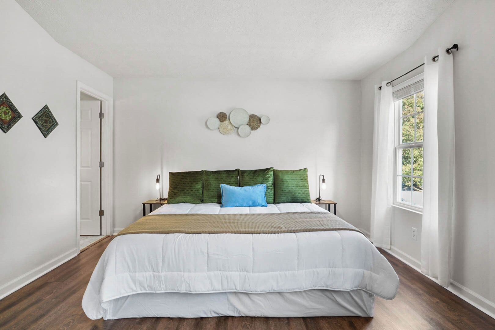 Une chambre à coucher avec un grand lit, deux tables de chevet, un élément décoratif mural et une fenêtre avec des rideaux.
