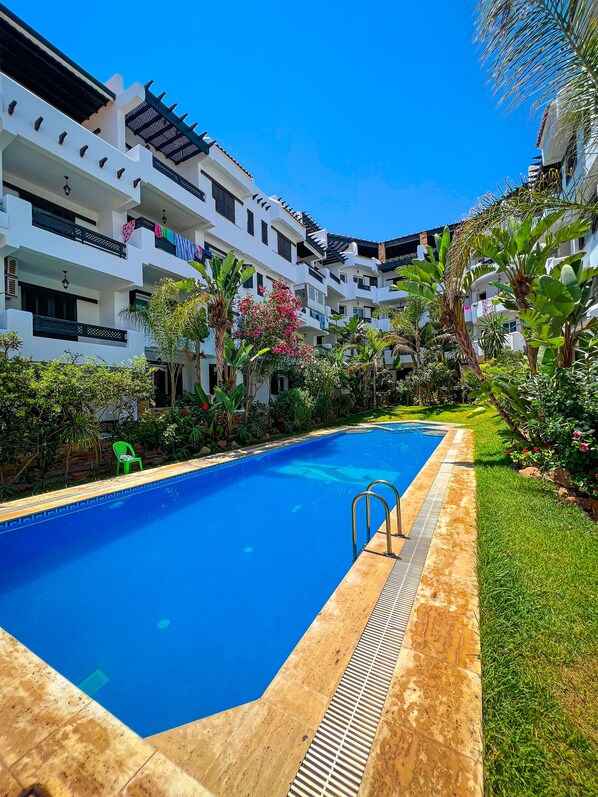 A swimming pool surrounded by lush greenery and white buildings with balconies.