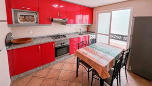 Una cocina con armarios rojos, estufa a gas, pileta y una mesa de comedor con sillas.